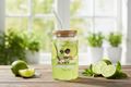 Jar with a straw lid, lime slices, and a garden-themed graphic on a wooden surface with plants in the background.