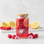 Jar of red lemonade with floral design and straw, surrounded by lemons and raspberries on a light background