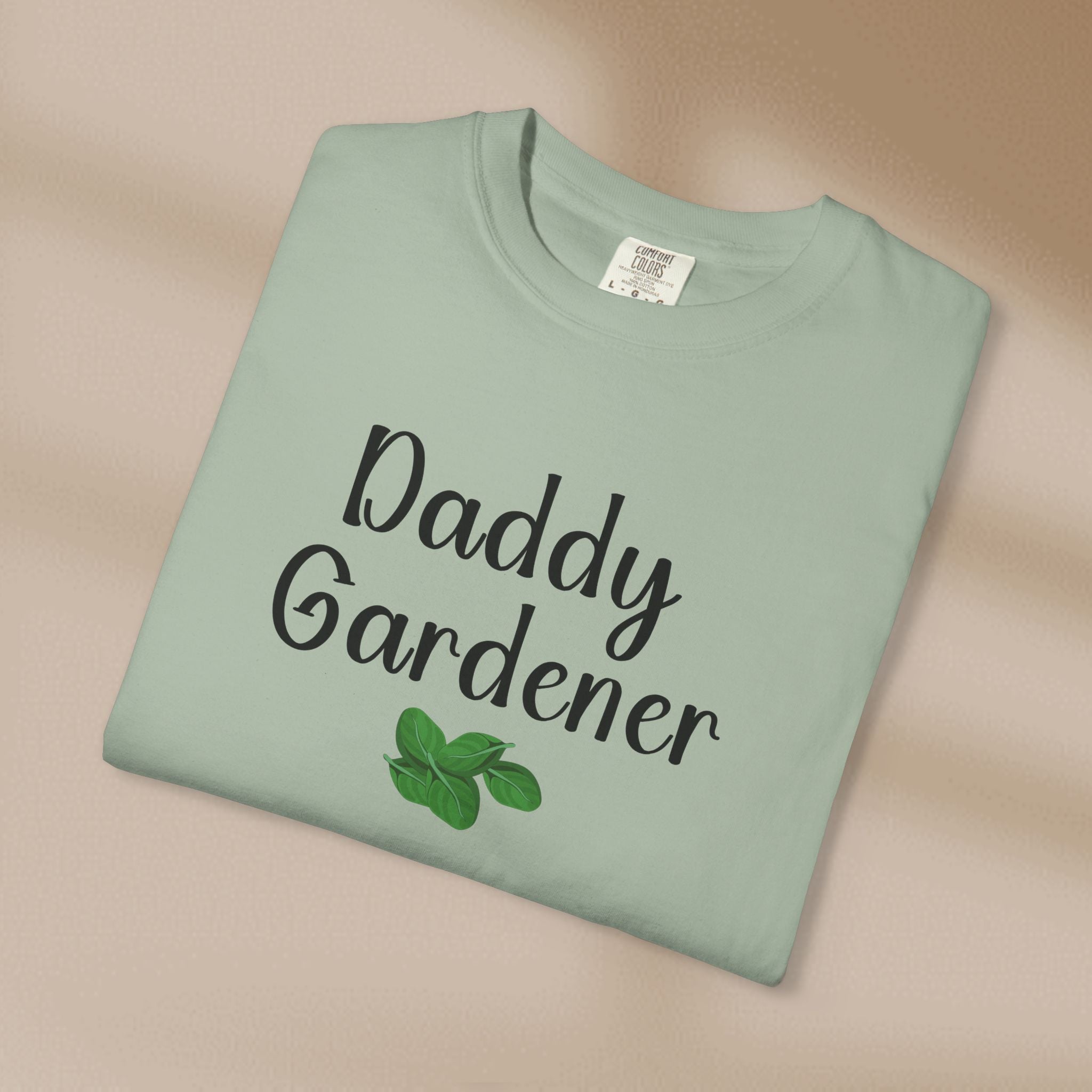 Folded green t-shirt with 'Daddy Gardener' text and leaf graphics on a beige background