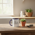 White mug with blue interior and 'Life & Garden' text on a wooden table with a potted plant and gardening tools.