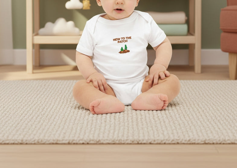 Baby wearing a onesie with text and graphics, surrounded by toys on a beige background