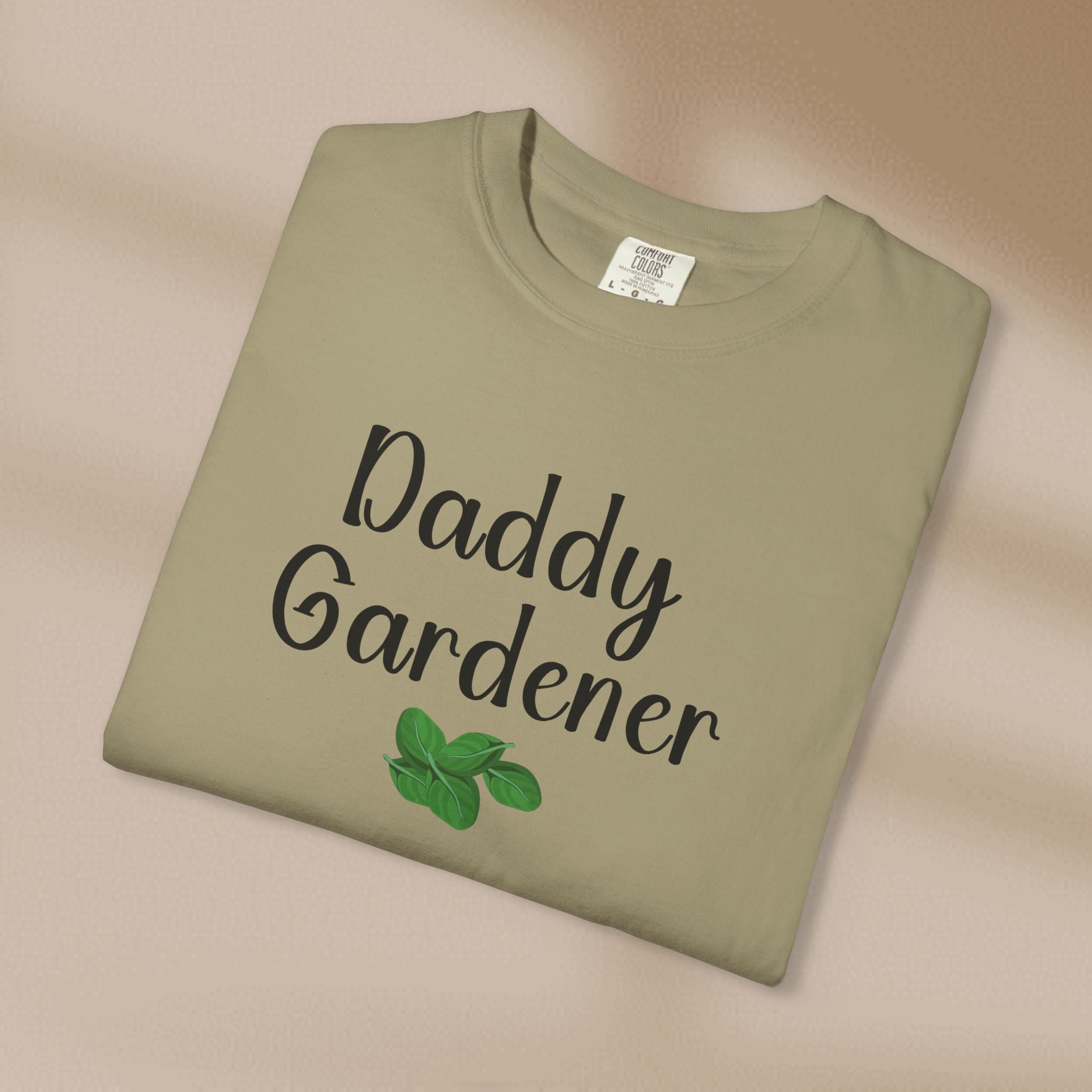 Folded green t-shirt with 'Daddy Gardener' text and leaf design on a beige background