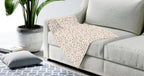 Gray sofa with a patterned blanket, plant, and rug in a living room setting