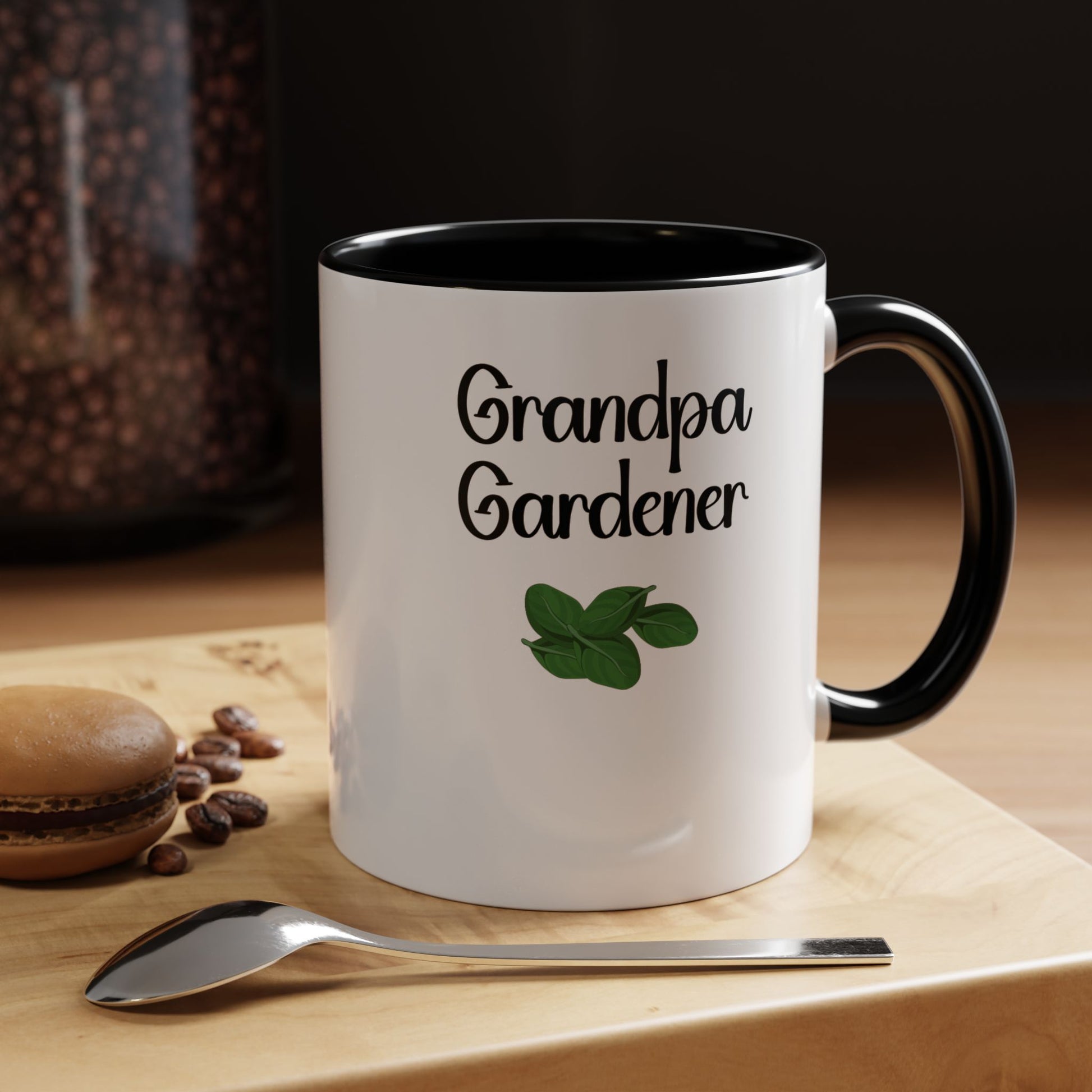 Mug with 'Grandpa Gardener' text and green leaf design on a wooden surface with coffee beans and a spoon.