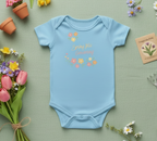 Baby in a blue onesie with floral designs sitting on the floor, coloring in a book with crayons.