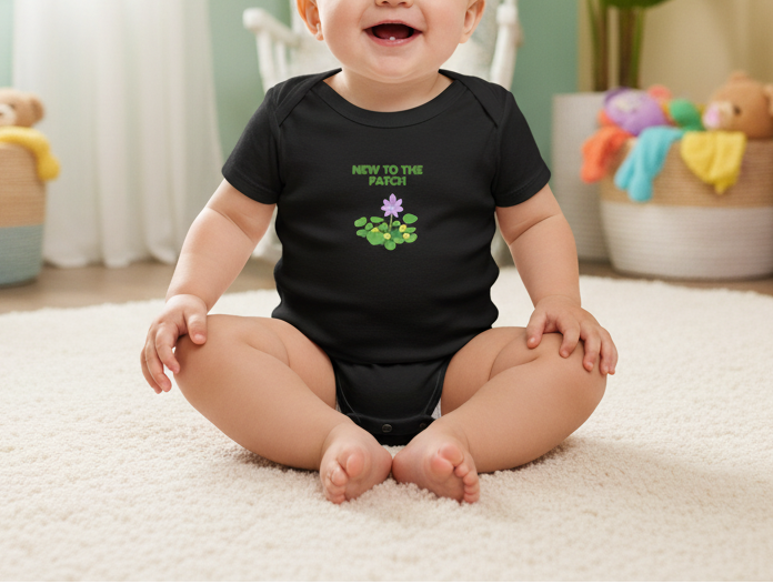 Baby wearing a black onesie with a design and text, sitting on a carpeted floor.