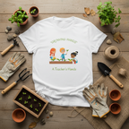 White t-shirt with 'Growing Hands, A Teacher's Hands' design on a wooden surface with gardening tools and plants.