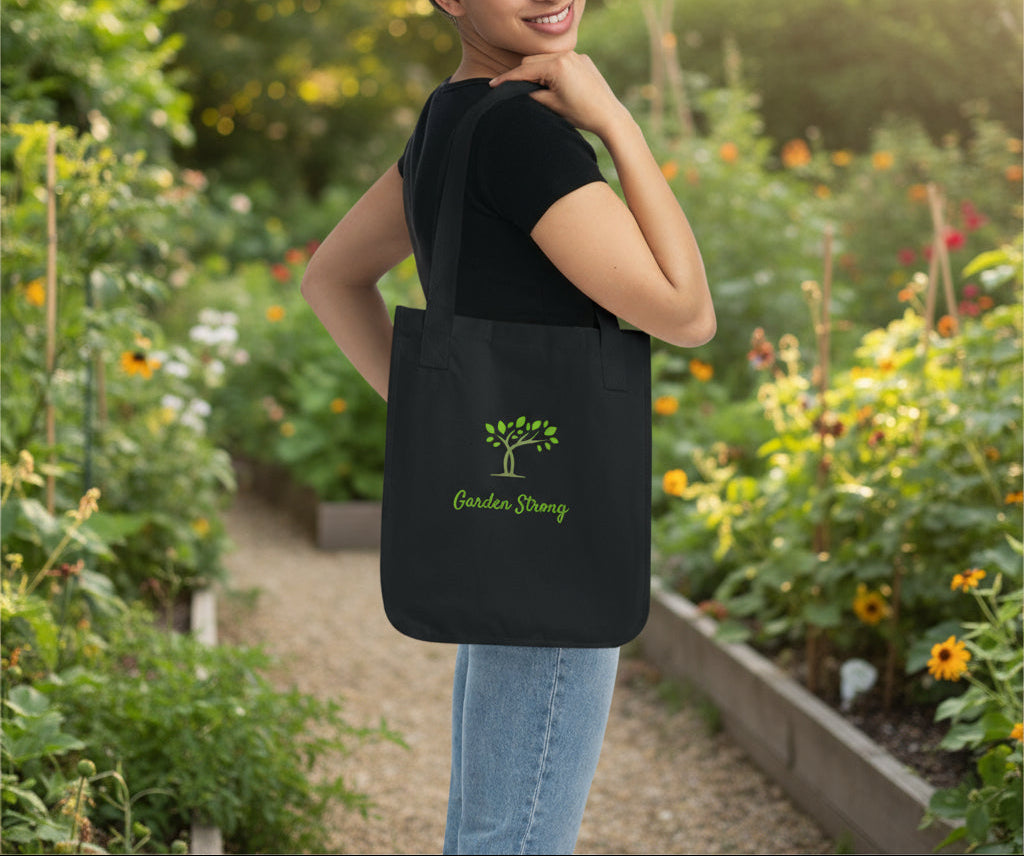 Woman carrying a black tote bag with 'Garden Strong' text and tree design on a white background
