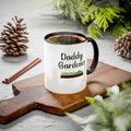 Mug with 'Daddy Gardener' text on a wooden board with pinecones and cinnamon sticks.