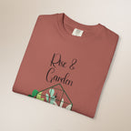 Folded terracotta-colored t-shirt with 'Rise & Garden' text and plant design on a beige background
