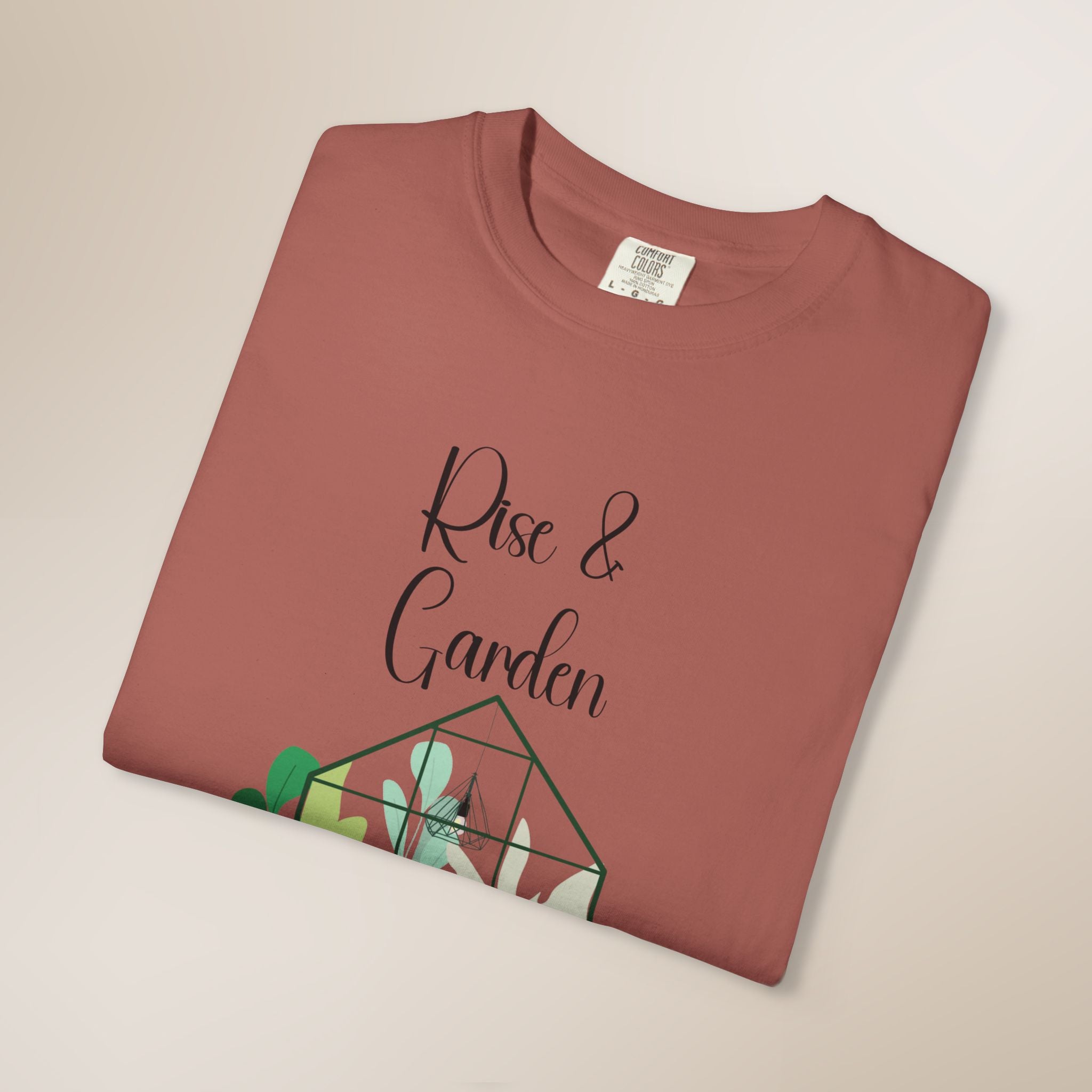Folded terracotta-colored t-shirt with 'Rise & Garden' text and plant design on a beige background