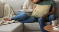 Two people sitting on a couch with a floral pillow, one person holding a cup.