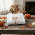 White sweatshirt with 'Fall in Gardening' design on a wooden table with pumpkins and leaves.