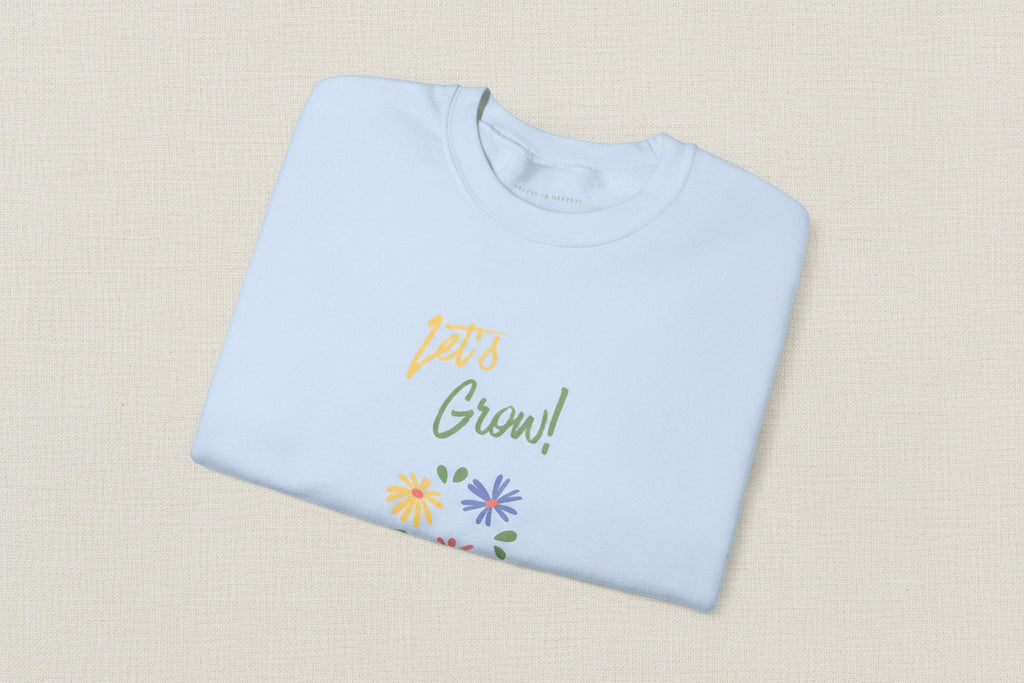 Folded light blue shirt with 'Let's Grow!' text and floral designs on a white background