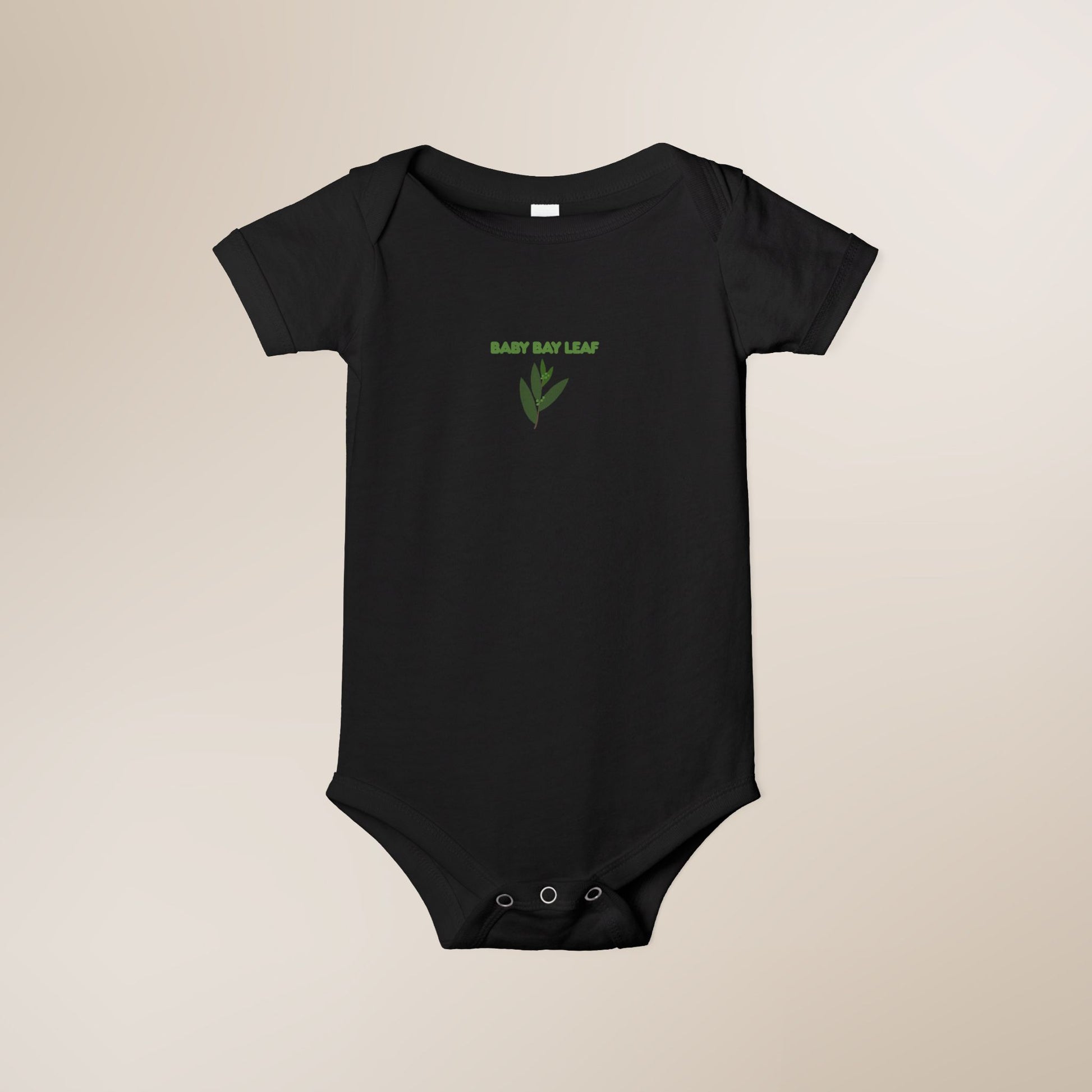 Black baby onesie with green text and leaf design on a beige background