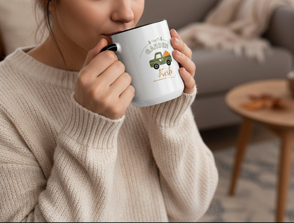 White mug with black interior and handle featuring a green truck and pumpkins design on a beige background.