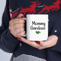 Person holding a white mug with 'Mommy Gardener' text, wearing a dark sweater with red deer design.