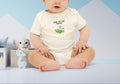 Baby wearing a white onesie with text and graphics, sitting on a blue surface with a light blue background