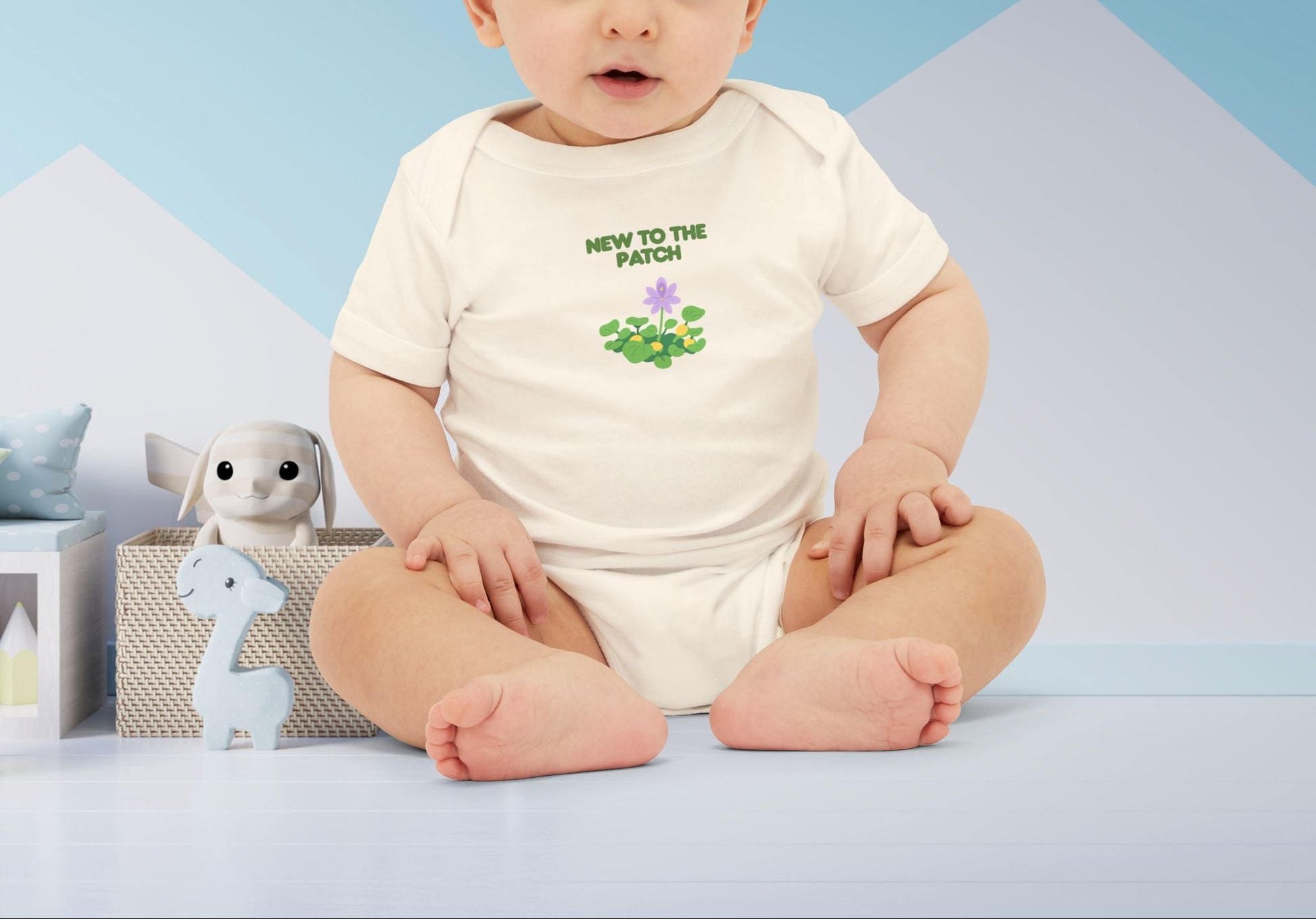 Baby wearing a white onesie with text and graphics, sitting on a blue surface with a light blue background