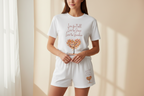 Person wearing a white t-shirt and shorts set with a tree design and text.