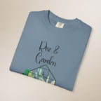 Folded blue t-shirt with 'Rise & Garden' text and cactus design on a beige background