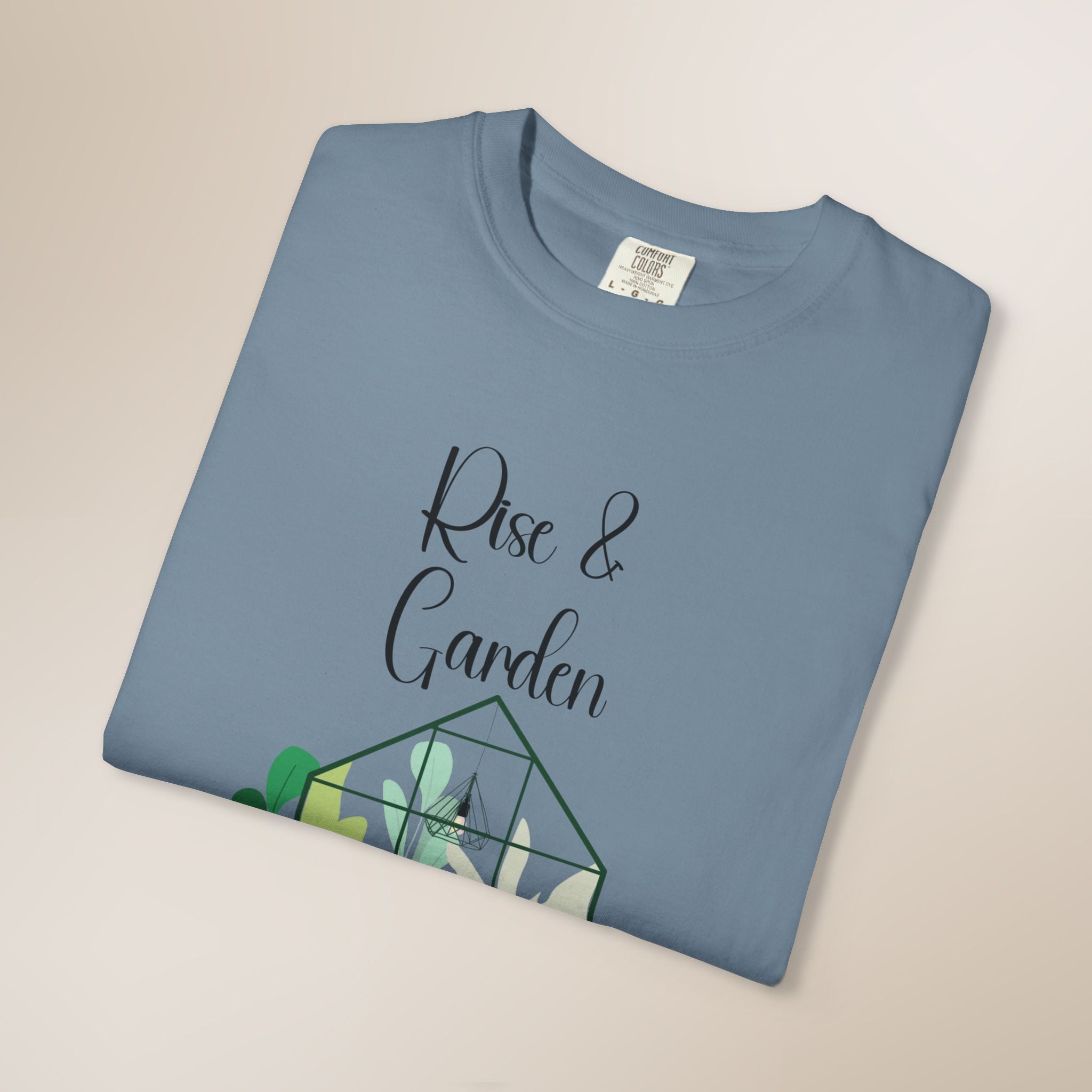 Folded blue t-shirt with 'Rise & Garden' text and cactus design on a beige background