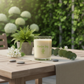 Candle labeled 'Garden Joy' on a wooden table with plants and stones in the background