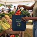 Person holding a blue tote bag filled with fresh produce at an outdoor market.
