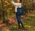 Woman picking apples in an orchard with a 'Mummy Gardener' tote bag.