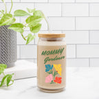Jar labeled 'Mommy Gardener' with colorful flowers on a white surface with a plant in the background.