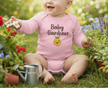 Baby in a pink 'Baby Gardener' onesie sitting in a garden with flowers and plants.