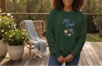 Person wearing a green sweatshirt with floral designs and text, standing on a wooden deck with plants and furniture.