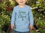 Child wearing a light blue sweatshirt with 'Grow a Little Cheer' text in a garden setting