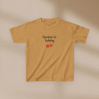 Mustard yellow t-shirt with 'Gardener in Training' text and tomato graphics on a beige background