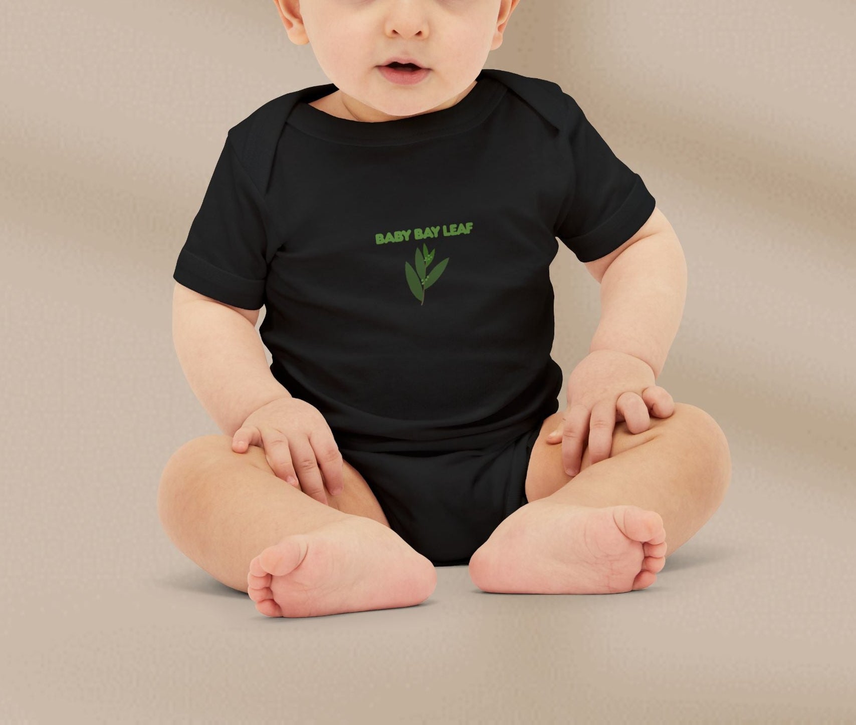 Baby wearing a black onesie with 'Baby Bay Leaf' text and leaf graphic on a beige background