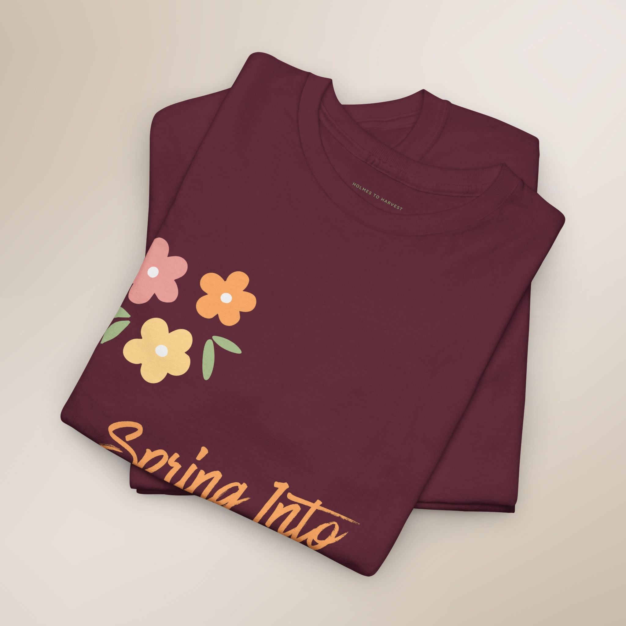 Folded maroon t-shirt with floral design and 'Spring Into' text on a beige background