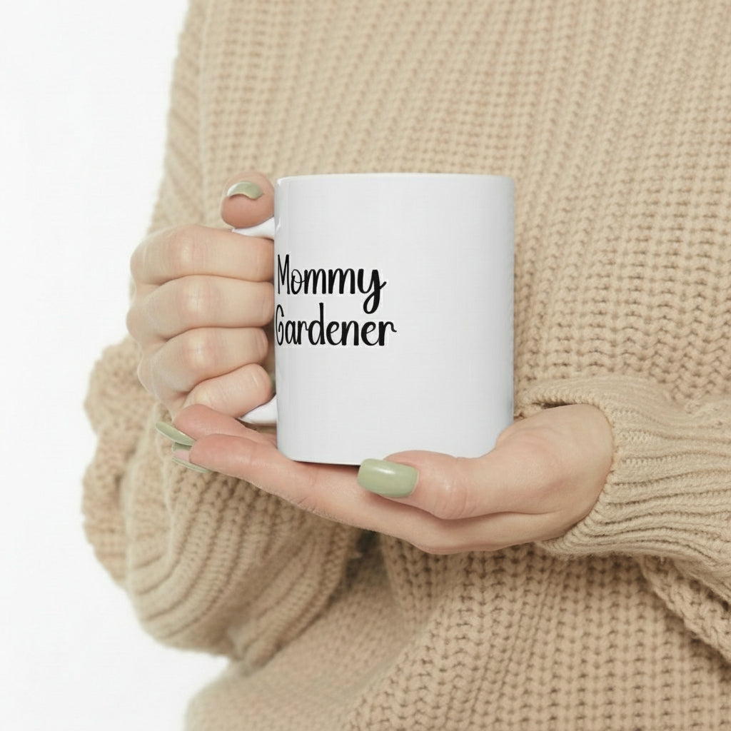 Person holding a white mug with 'Mommy Gardener' text, wearing a beige sweater.