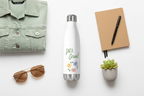 Green jacket, white water bottle with 'Let's Grow!' text, sunglasses, notebook, pen, and small plant on a white background