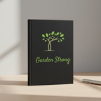 Black notebook with 'Garden Strong' and a tree design on a wooden surface.