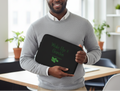 Man holding a black laptop case with 'Wake Up & Garden' text in a bright room.