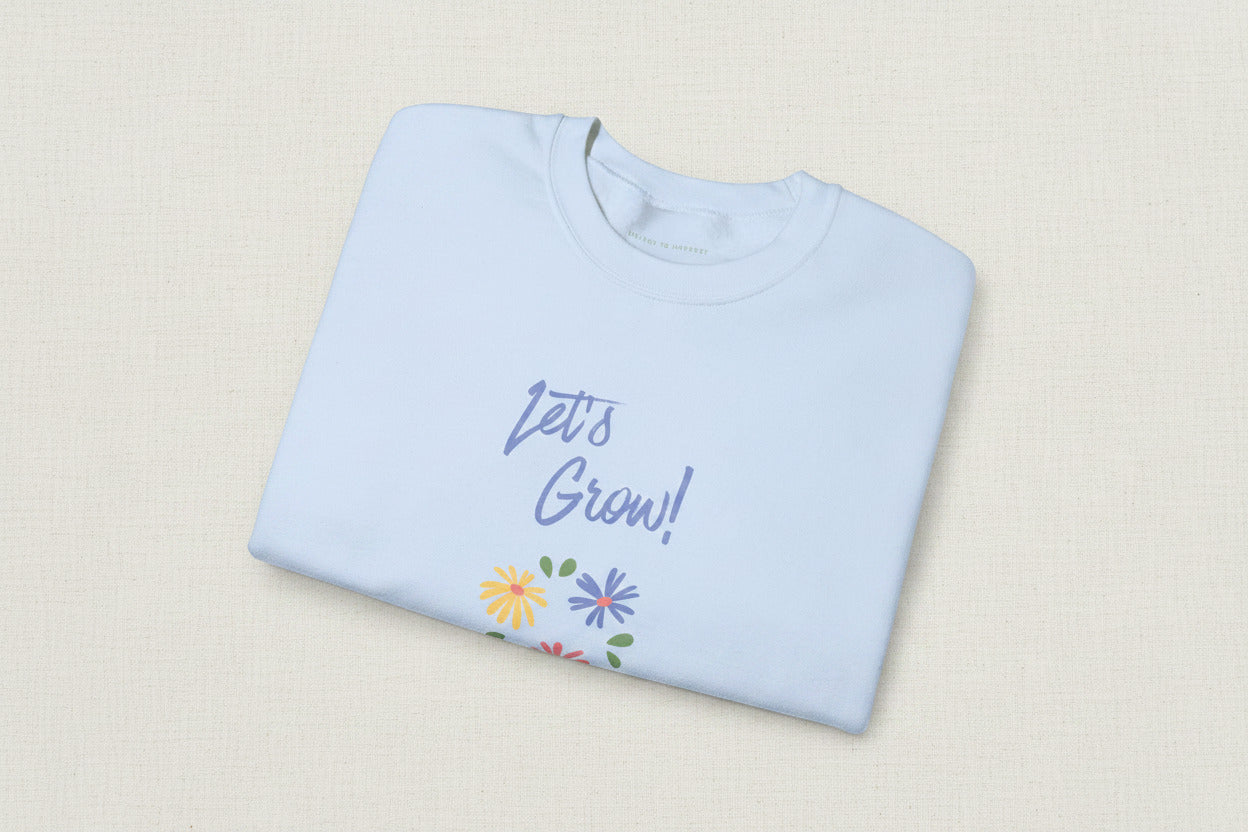 Folded light blue sweatshirt with 'Let's Grow!' text and floral designs on a white background