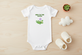 White baby onesie with 'New to the Patch' text and plant graphics on a wooden surface with baby shoes and a small plant.
