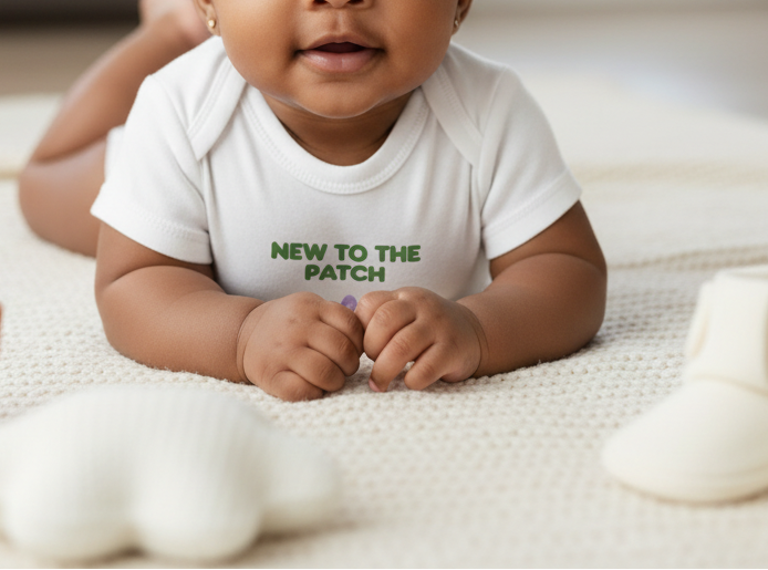Baby wearing a white onesie with 'NEW TO THE PATCH' text on a light background