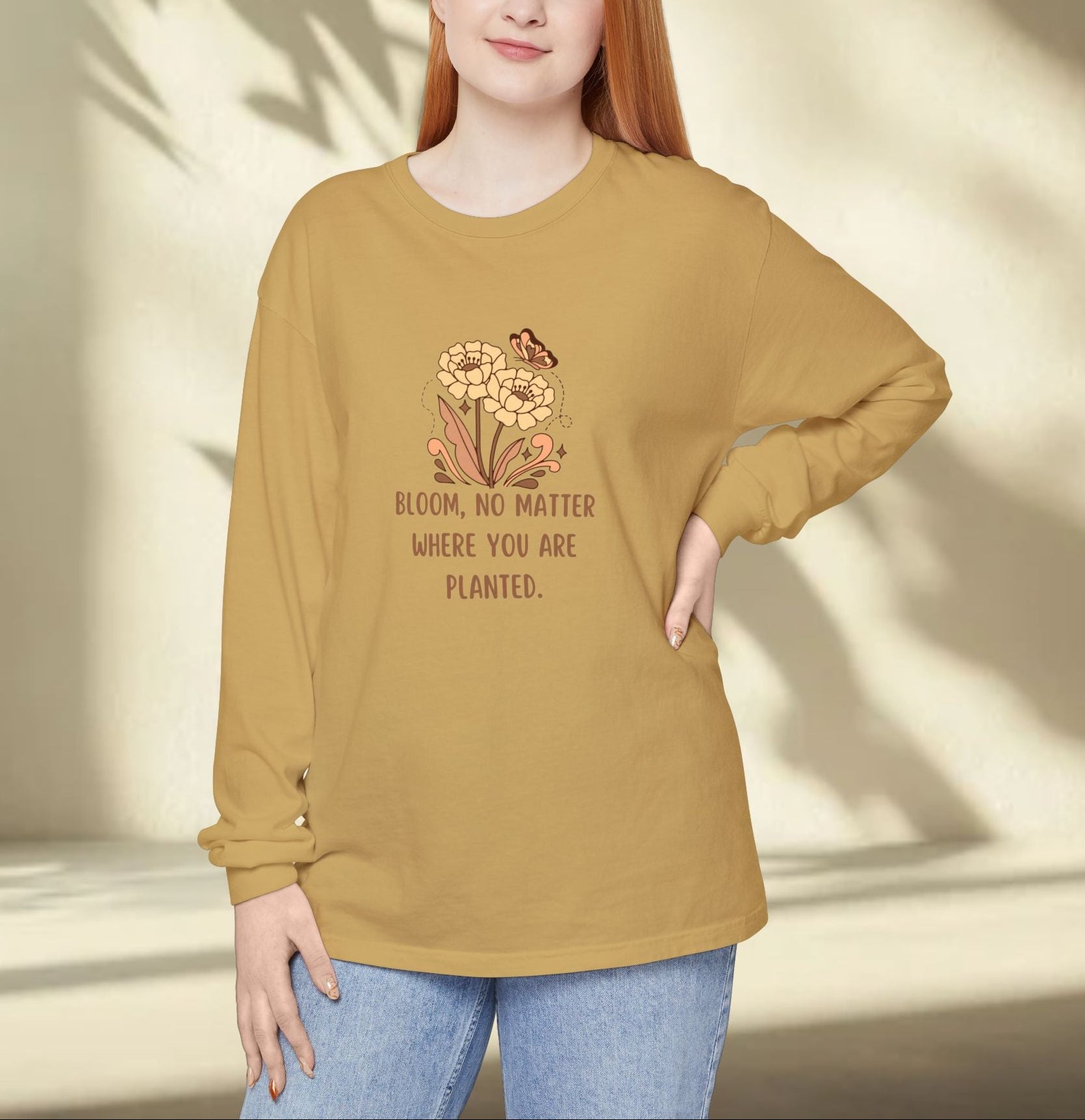 Woman wearing a mustard yellow long-sleeve shirt with a floral design and text, standing against a neutral background.