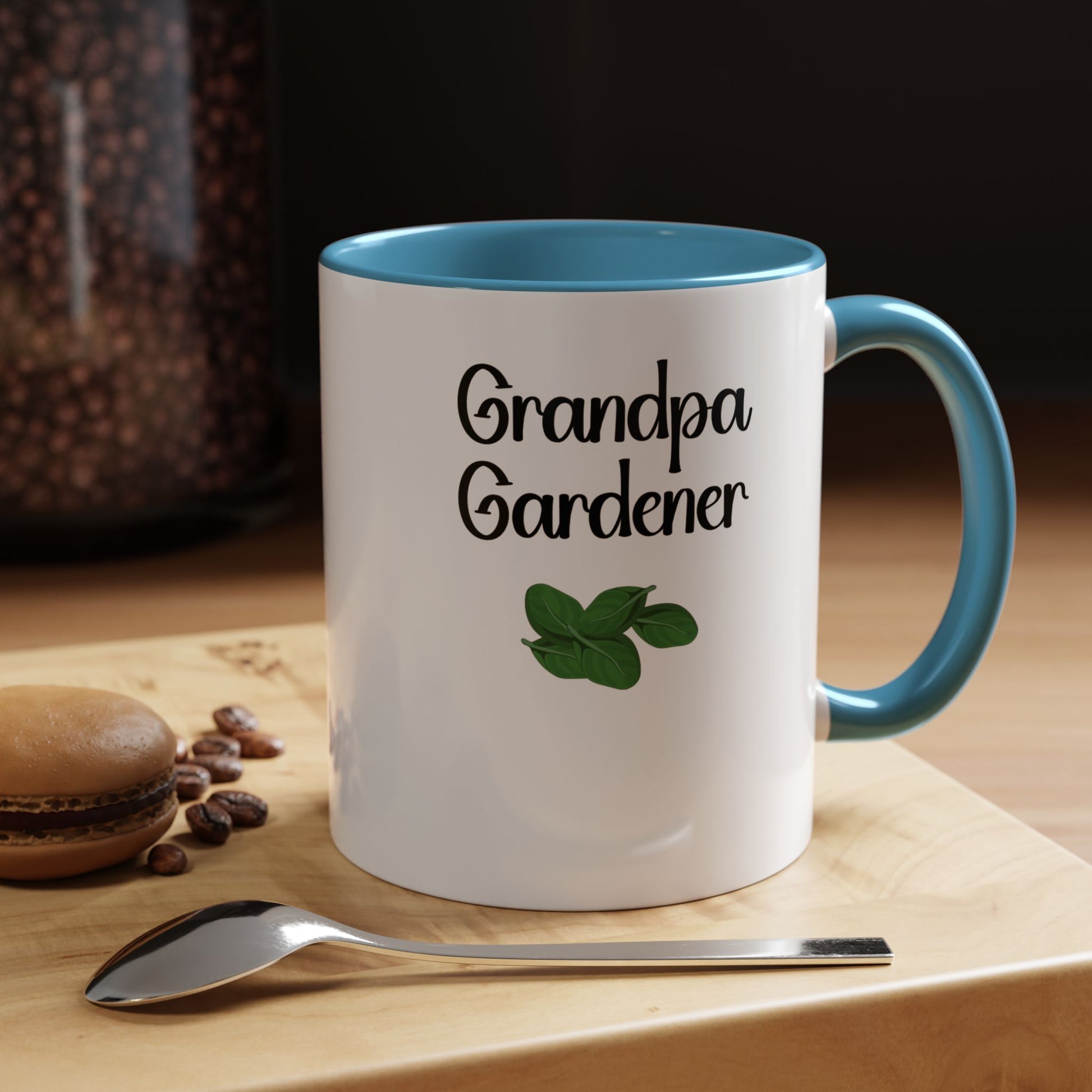 Mug with 'Grandpa Gardener' text and green leaf design on a wooden surface with coffee beans and a spoon.