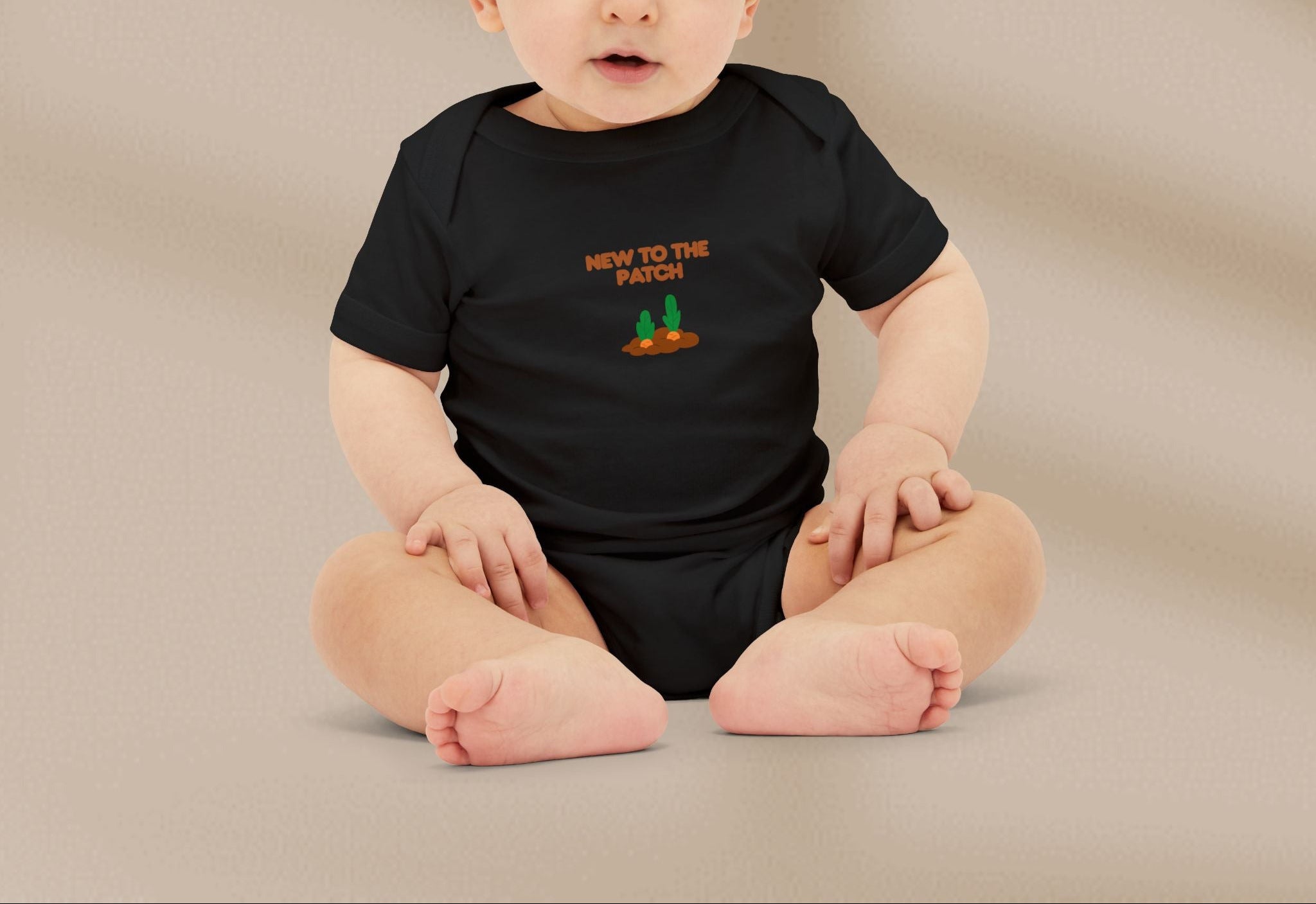 Baby wearing a black onesie with text and graphics on a beige background