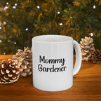 White mug with 'Mommy Gardener' text in front of a Christmas tree and pinecones.