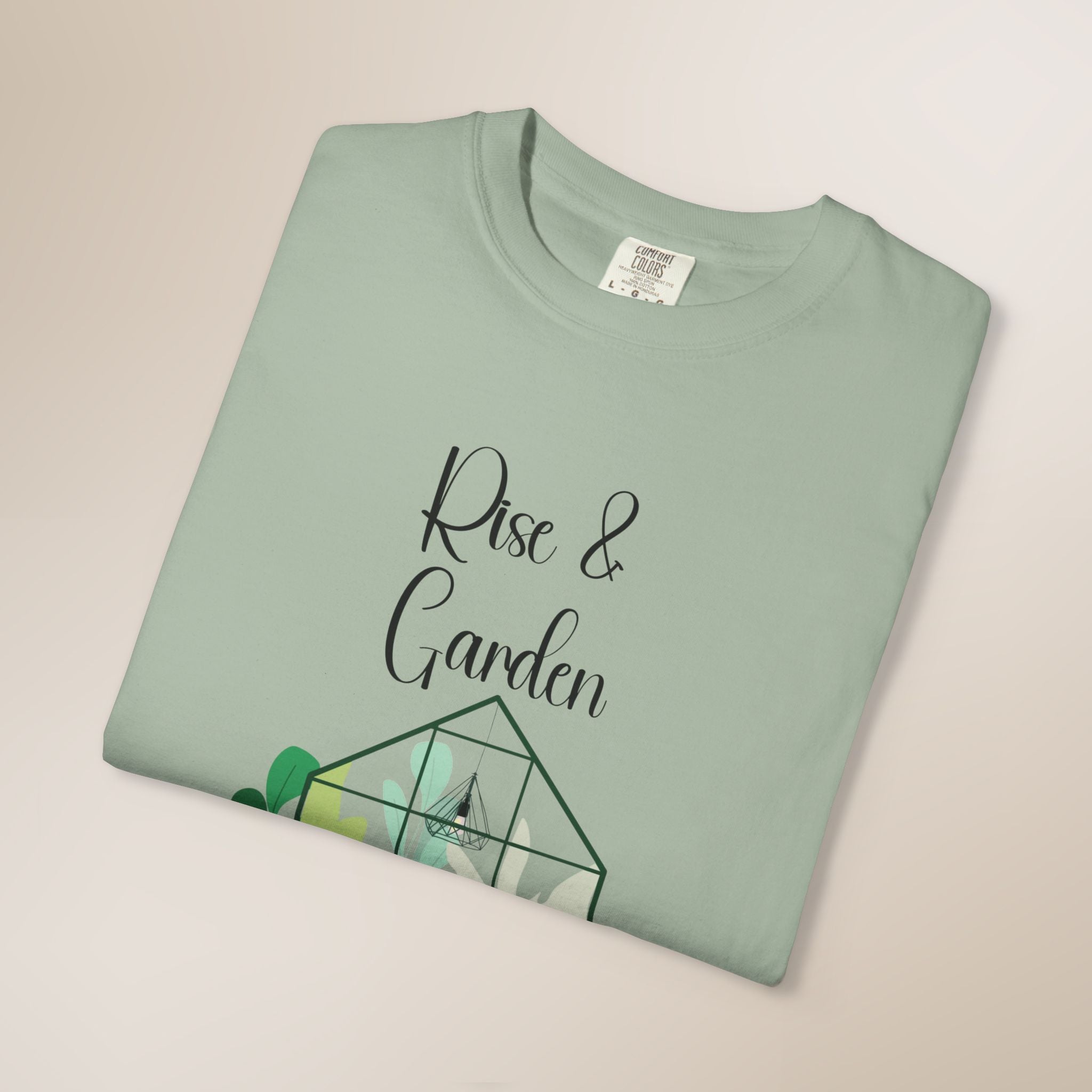 Folded mint green t-shirt with 'Rise & Garden' text on a beige background