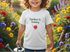 Child wearing a 'Gardener in Training' t-shirt in a garden setting with flowers.