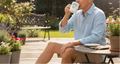 Person sitting outdoors on a wooden deck, drinking from a mug.
